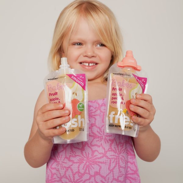 Smiling toddler holding food pouches fitted with silicone pouch toppers by Junary